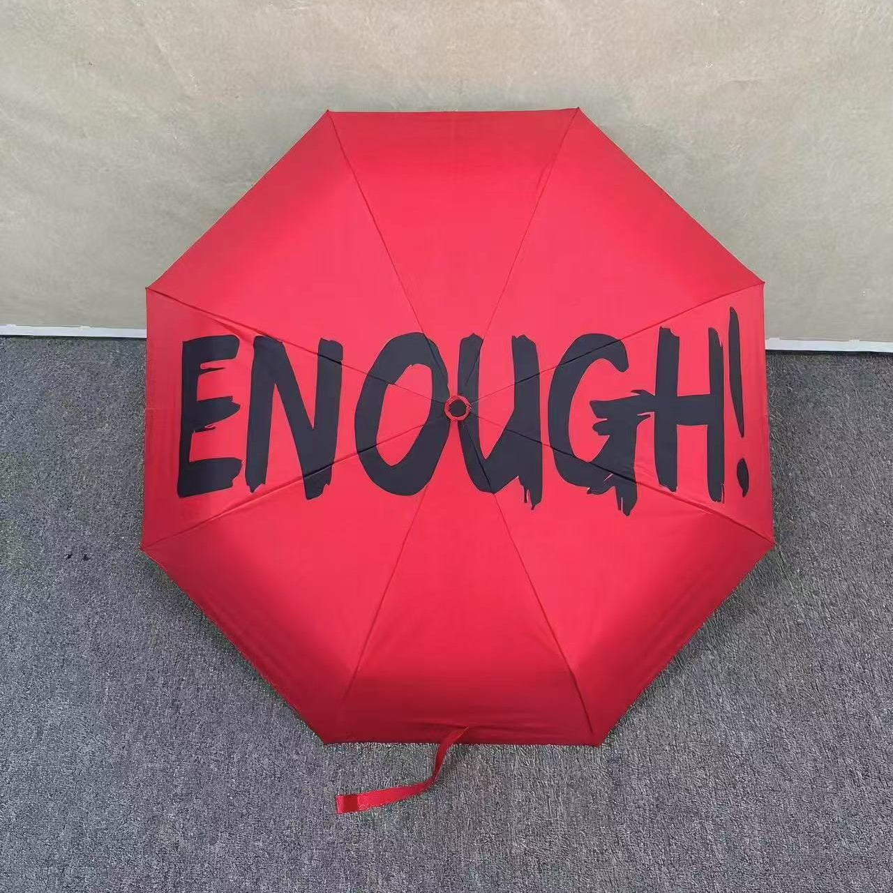 Red umbrella with 'ENOUGH!' text on a neutral background. UV coated for sun protection.