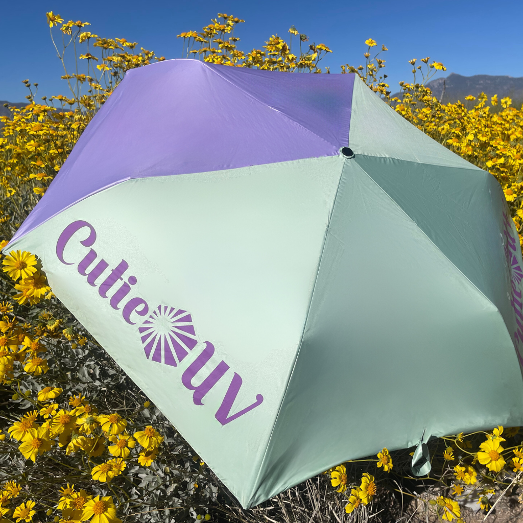 Photo of CutieUV sun umbrella in a field of yellow flowers with mountains behind